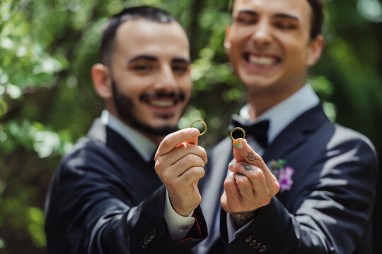 happy and blurred gay men holding wedding rings in hands.