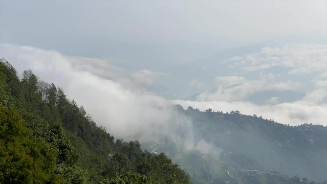 A time-lapse of clouds flowing over the ridge of a mountain and into the valley.