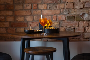 Traditional italian aperitif with cheese, nuts and aperol spritz drink on the wooden table with blurred food on the background in a bar