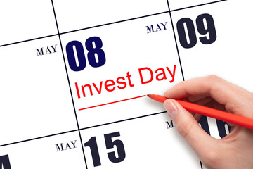 Hand drawing red line and writing the text Invest Day on calendar date May 8. Business and financial concept.