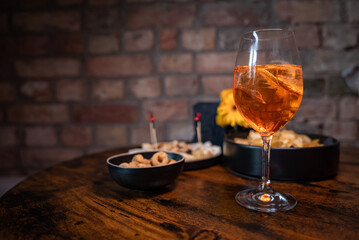Traditional italian aperitif with cheese, nuts and aperol spritz drink on the wooden table with blurred food on the background in a bar