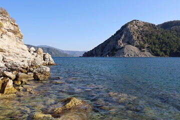 Picturesque view to rock cliff in Mediterranean sea. Summer coast with turquoise transparent water and green mountains