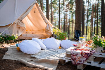 Beautiful white decor in boho style. Picnic in the nature, table, carpets, wigwam, tent, pillows in...
