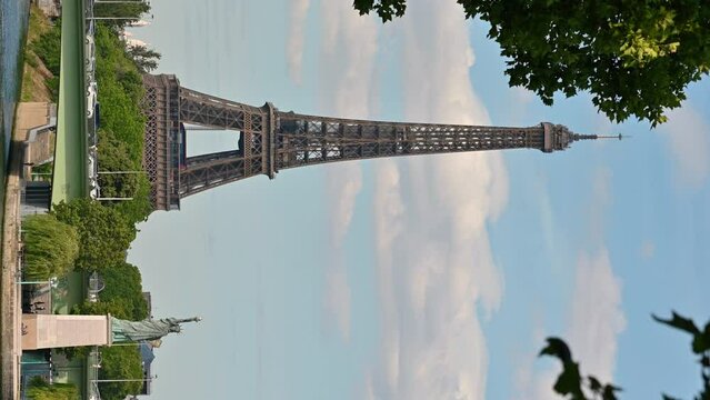 Paris, France. June 2022. Amazing footage that collects two symbols of France: between the leaves moved by the wind the Eiffel Tower and the statue of liberty at the base. Vertical format.