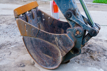Closeup of front bucket of earth excavator on surface of city street during road repair project