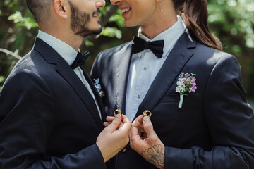 cropped view of happy gay couple holding wedding rings in hands.