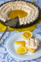 Homemade yellow shortbread pie with lemon cream and meringue on blue tablecloth and lemons