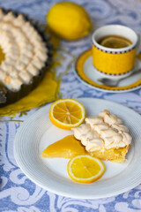 Homemade yellow shortbread pie with lemon cream and meringue on blue tablecloth and lemons