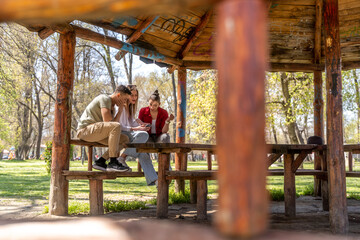 Obraz na płótnie Canvas Happy friends watching a smart phone sitting on a bench in a park