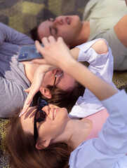 Group of three people using smart phones while lying on green laws