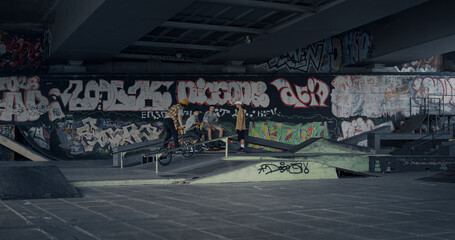 Extreme man performing jump stunt on bmx bike at skate park with graffiti.