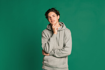 Fototapeta premium Studio shot of young boy, teen in casual style clothes looking at camera isolated over green studio background. Back to school, emotions, youth, fashion concept