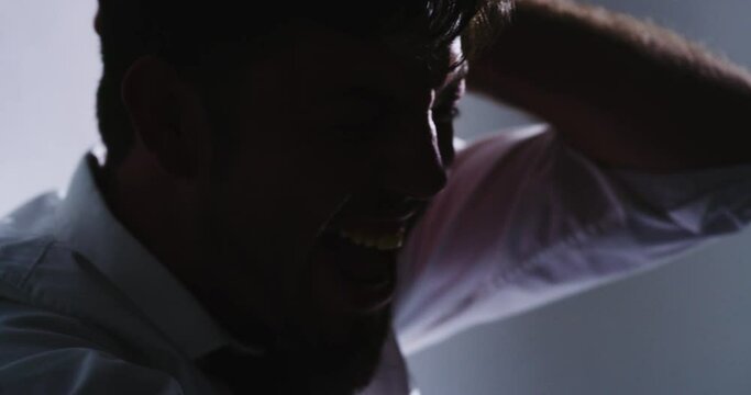 Closeup silhouette of an angry man screaming alone in a room. Stressed male office worker having a mental breakdown from overwork. Mentally ill person suffering from severe paranoia or anxiety.