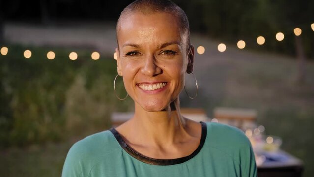 Portrait looking at the camera of a shaved head happy woman. Smiling lady alone outdoors at night