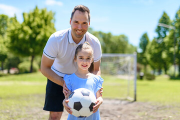 Young father with his little daughter playing football on football pitch