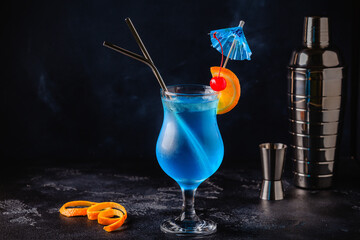 gGass of blue lagoon cocktail decorated with orange and cherry at festive bar counter background. © tbralnina