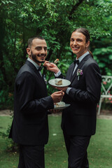 pleased gay newlyweds in formal wear holding wedding cake.