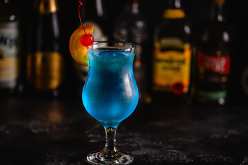 gGass of blue lagoon cocktail decorated with orange and cherry at festive bar counter background.