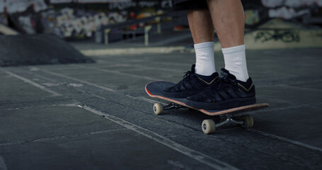Fototapeta premium Active man practicing skateboard at skate park with graffiti on wall. 