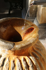 An old large clay jug into which flows a stream of water from a tap, close up