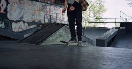 Young skater riding skateboard outside. Male legs in sneakers with board.