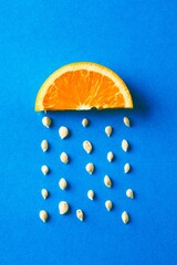 Creative food concept with an orange slice and seeds falling down like raindrops on blue background