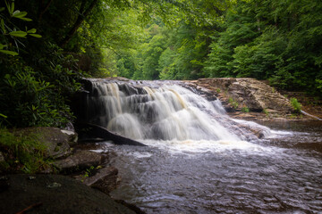Fototapeta premium Waterfall in forest cascading down rocks slow shutter speed horizontal
