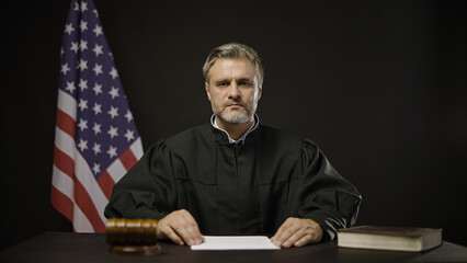 Strict male judge looking at camera in courtroom, American justice system