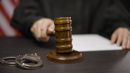 Male judge striking gavel for final verdict, handcuffs lying on court desk