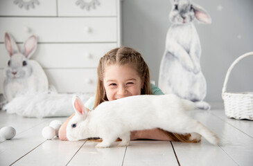 little smiling cute child with long blond hair and blue dress playing with rabbit in white studio