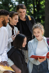 Student holding notebook near cheerful multicultural friends.