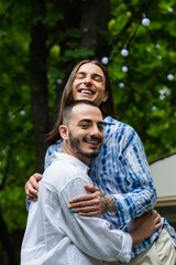 Naklejka na ściany i meble happy married gay couple smiling while hugging near blurred travel van.