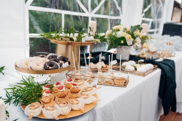 Closeup of banquet cakes and sweets ornamented with flowers and green leaves for the Communion