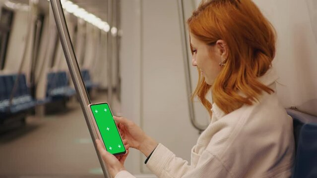 Tourist woman sitting down in a metro and scroll the green screen phone on the train. Using green screen smartphone for advertisement. Lifestyle and transportation concept. Passenger in subway.