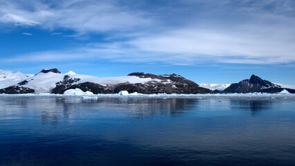 Icebergs floating at the base of a snow covered mountain, in the Southern Ocean, at Cierva Cove, Antarctica