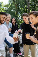 Multiethnic students with coffee to go looking at cellphone in park.