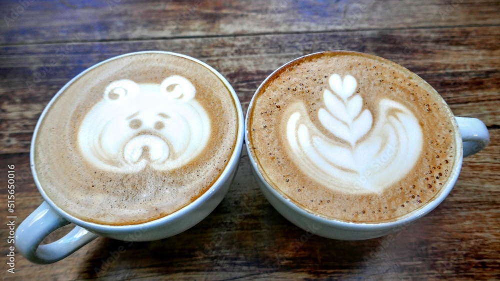 Sticker angle shot of two cups of coffee with drawn foam on a wooden table.