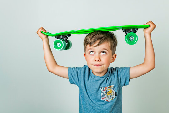 Little child sitting on a skateboard isolated on grey background