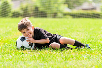 Cute boy playing football enjoying sport game outside