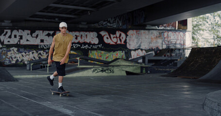 Young skater riding on skate board at skate park with graffiti wall background. © stockbusters