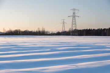 Snowy fields on cold and sunny winter evening. Forest and electricity towers in the background