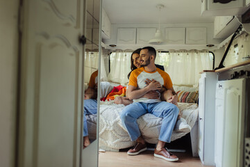 happy gay man with long hair hugging joyful boyfriend on bed in modern van.