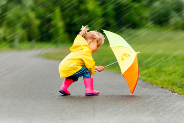 Happy funny child with multicolored umbrella under the summer raining day