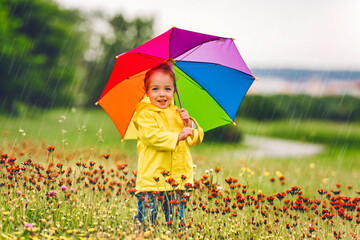 Happy funny child with multicolored umbrella under the summer raining day