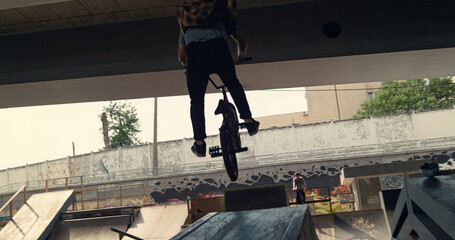 Active bmx rider training skills at skatepark. Biker racing up in ramp. 