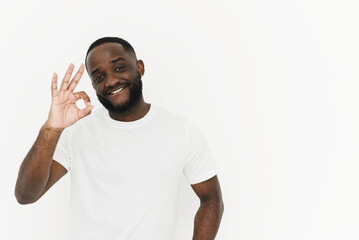 Smiling african american young man in white t-shirt showing ok gesture on white background with copy space