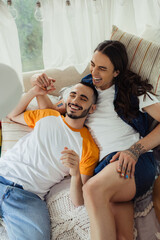 high angle view of smiling gay man with tattoos lying on bed with bearded boyfriend in modern van.