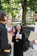 Cheerful asian student holding digital tablet near multiethnic friends in park.