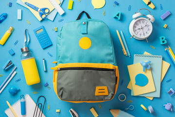 Back to school concept. Top view photo of blue schoolbag scattered stationery drink bottle and alarm clock on isolated blue background