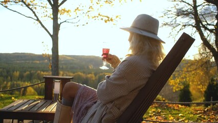 woman drinking wine sitting at sunset on the terrace overlooking the autumn forest